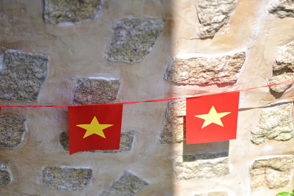 Vietnamese flag bunting hanging on a rustic stone wall in bright sunlight.